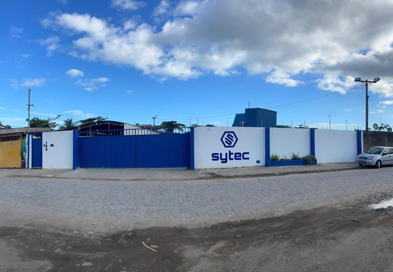 Fachada da base da Sytec em Macaé, com muro e portão azuis e o logo Sytec